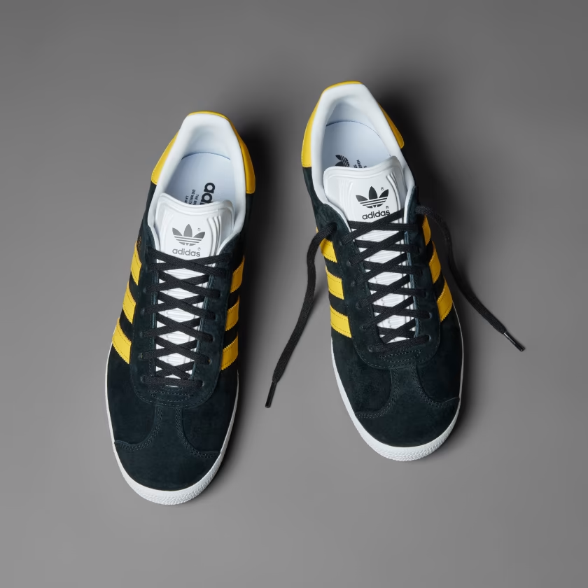 A pair of black adidas shoes with yellow stripes, black laces and a white tongue.